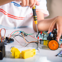 A kid building a robotic car using the KiddyPi robotics kit and electronics at a hands-on STEM summer camp for kids.